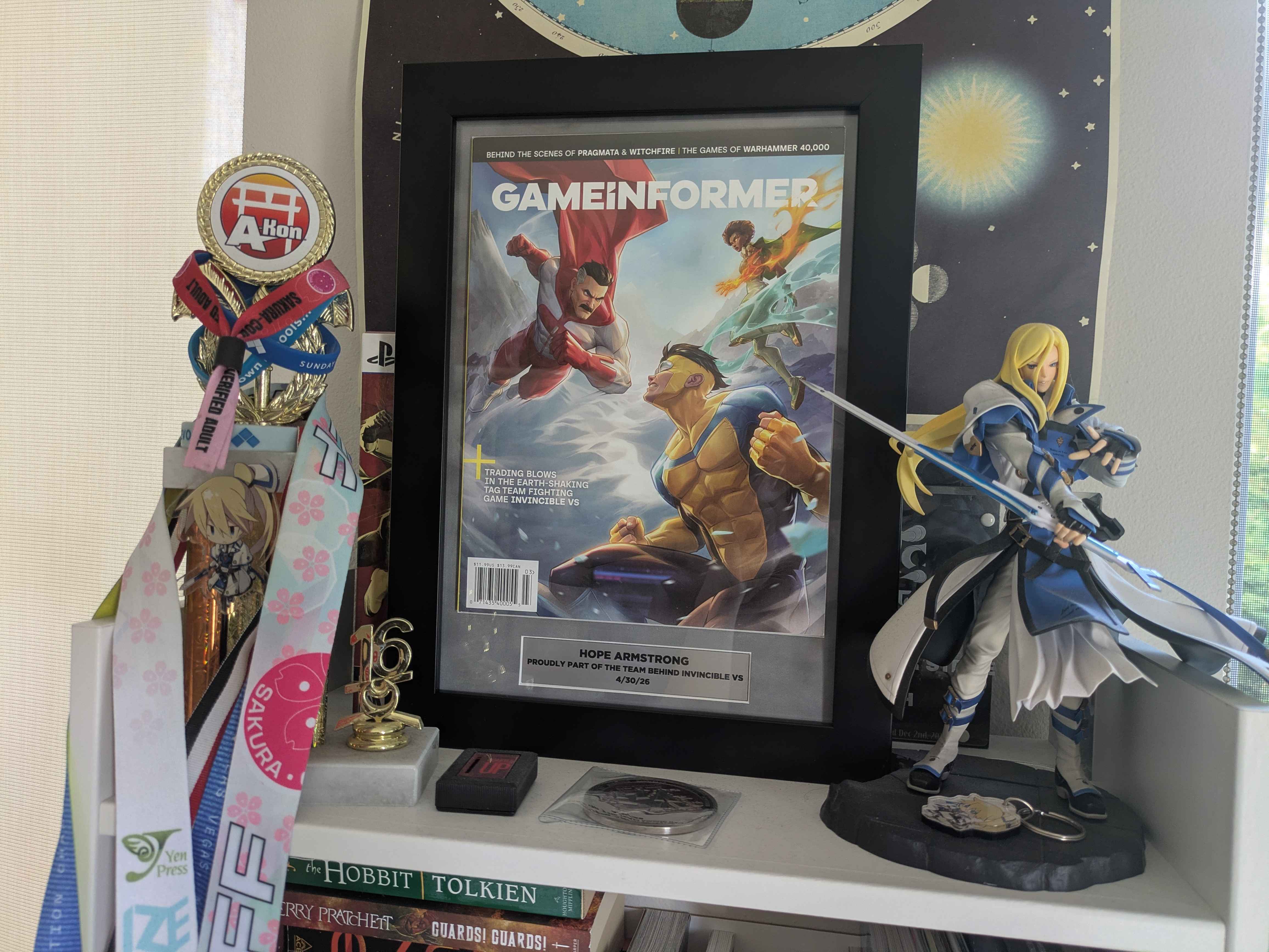 A framed copy of the Invincible VS issue of GameInformer. A plaque with the name Hope Armstrong is attached to the bottom.
      It's sitting on a white shelf next to other fighting game paraphernalia